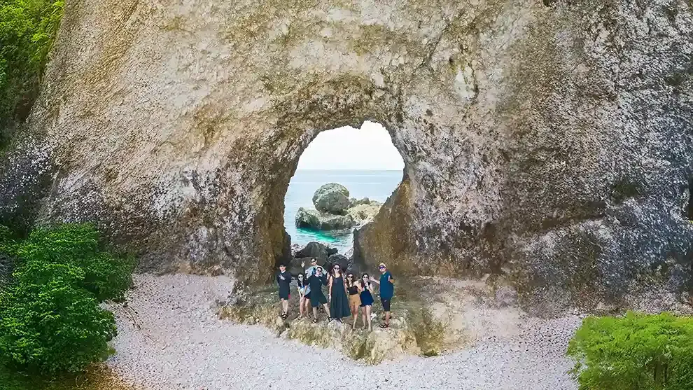 Travellers standing inside a limestone arch on a pebble beach