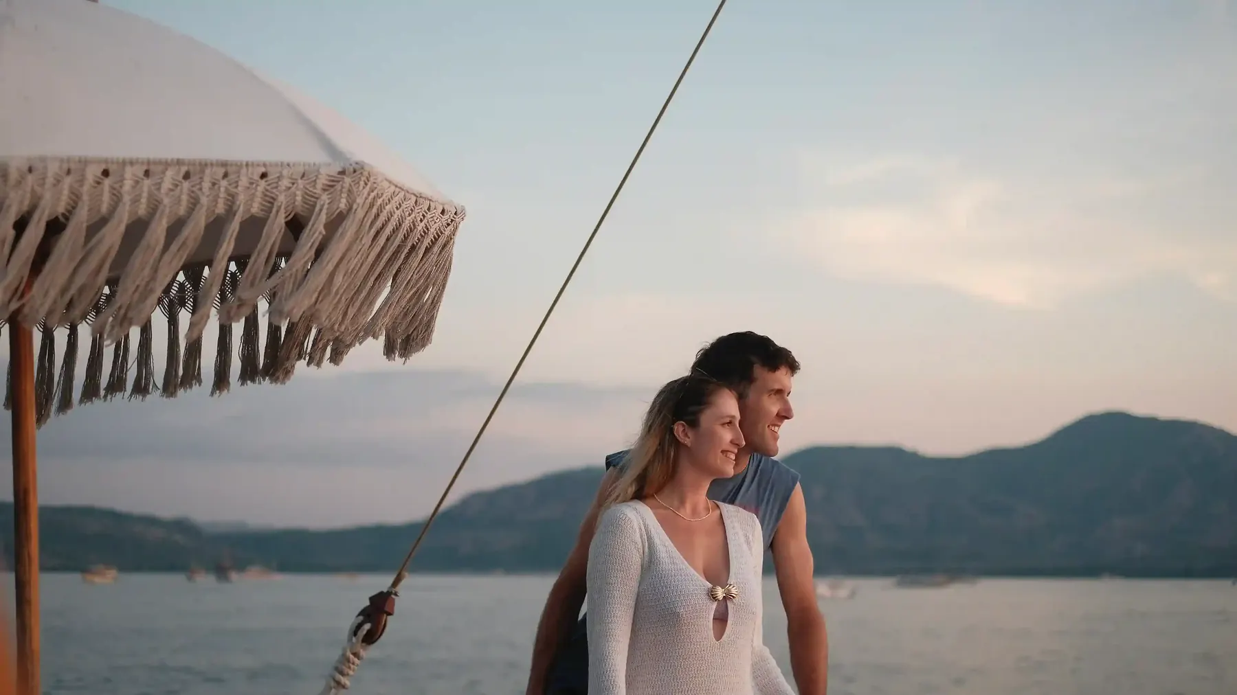 Couple on the bowsprit of a sailing yacht at dusk