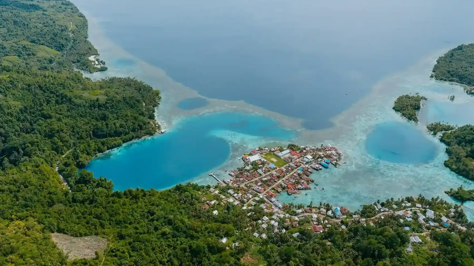 Aerial view of a coastal village between two blue lagoons and forested hills