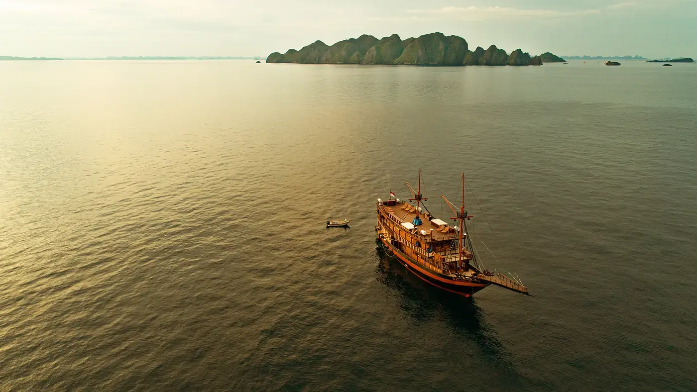 Wooden boat crossing a golden bay at sunset