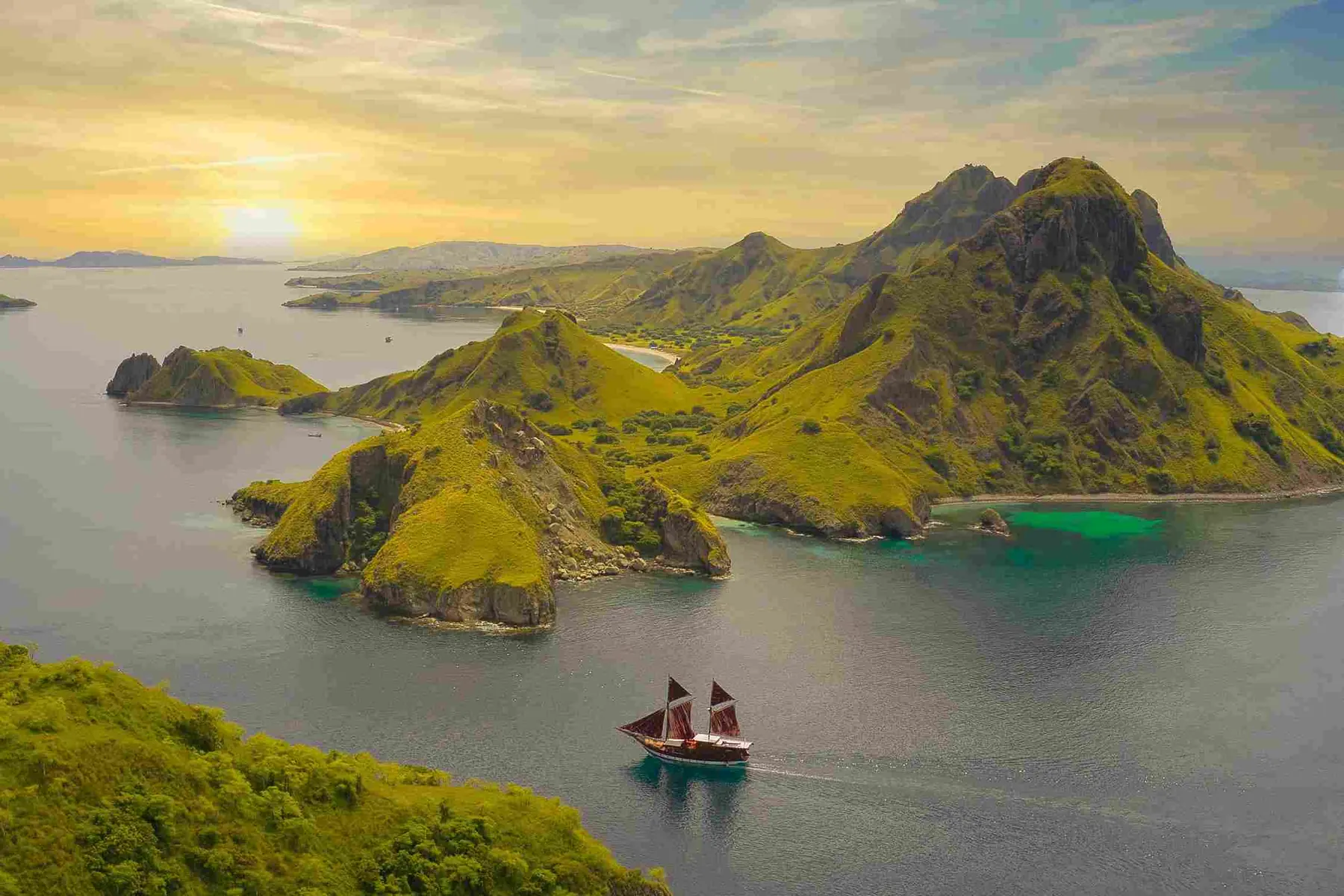 Wooden phinisi sailing beneath golden hills