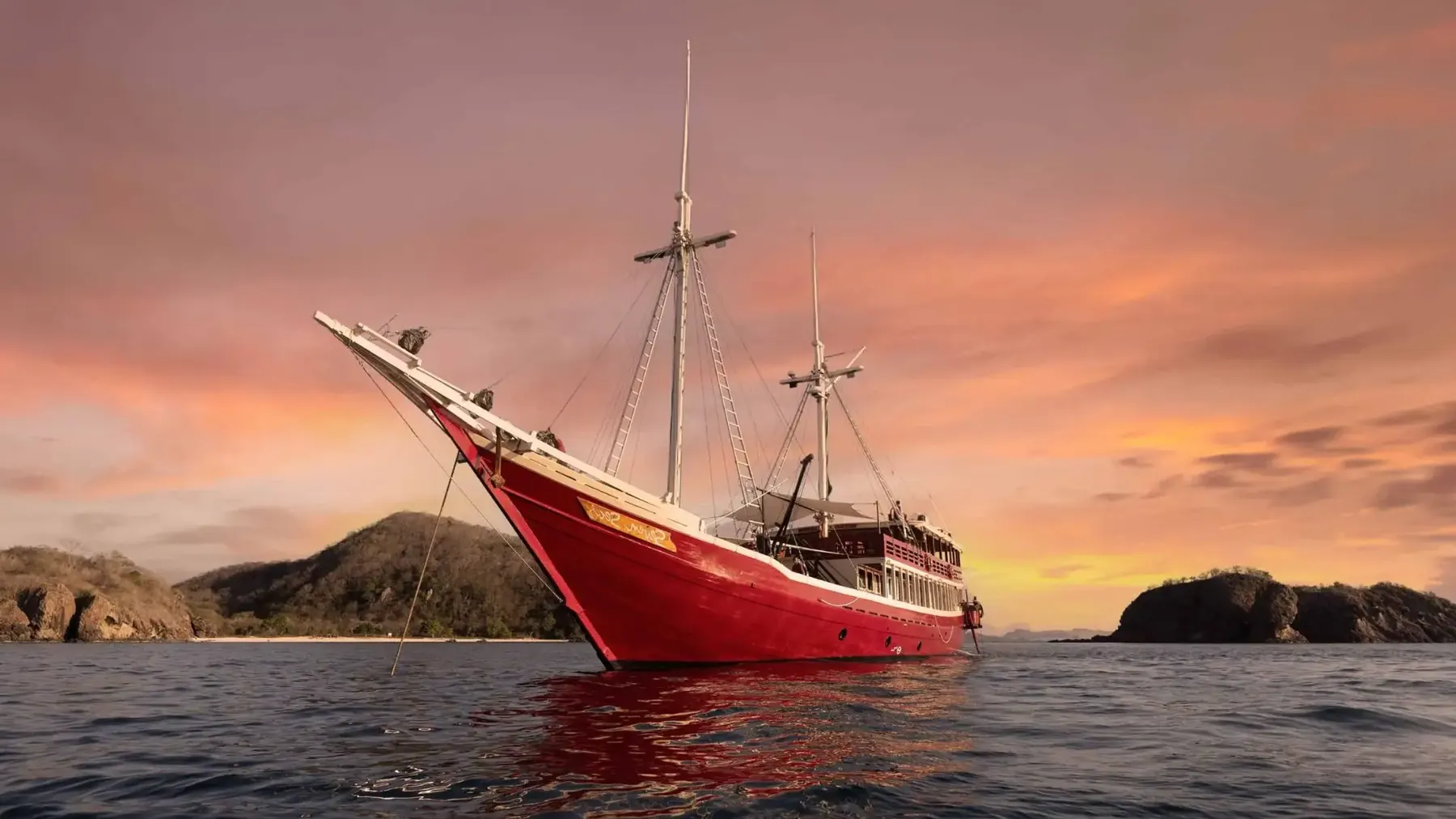 Red-hulled phinisi at anchor under a sunset sky