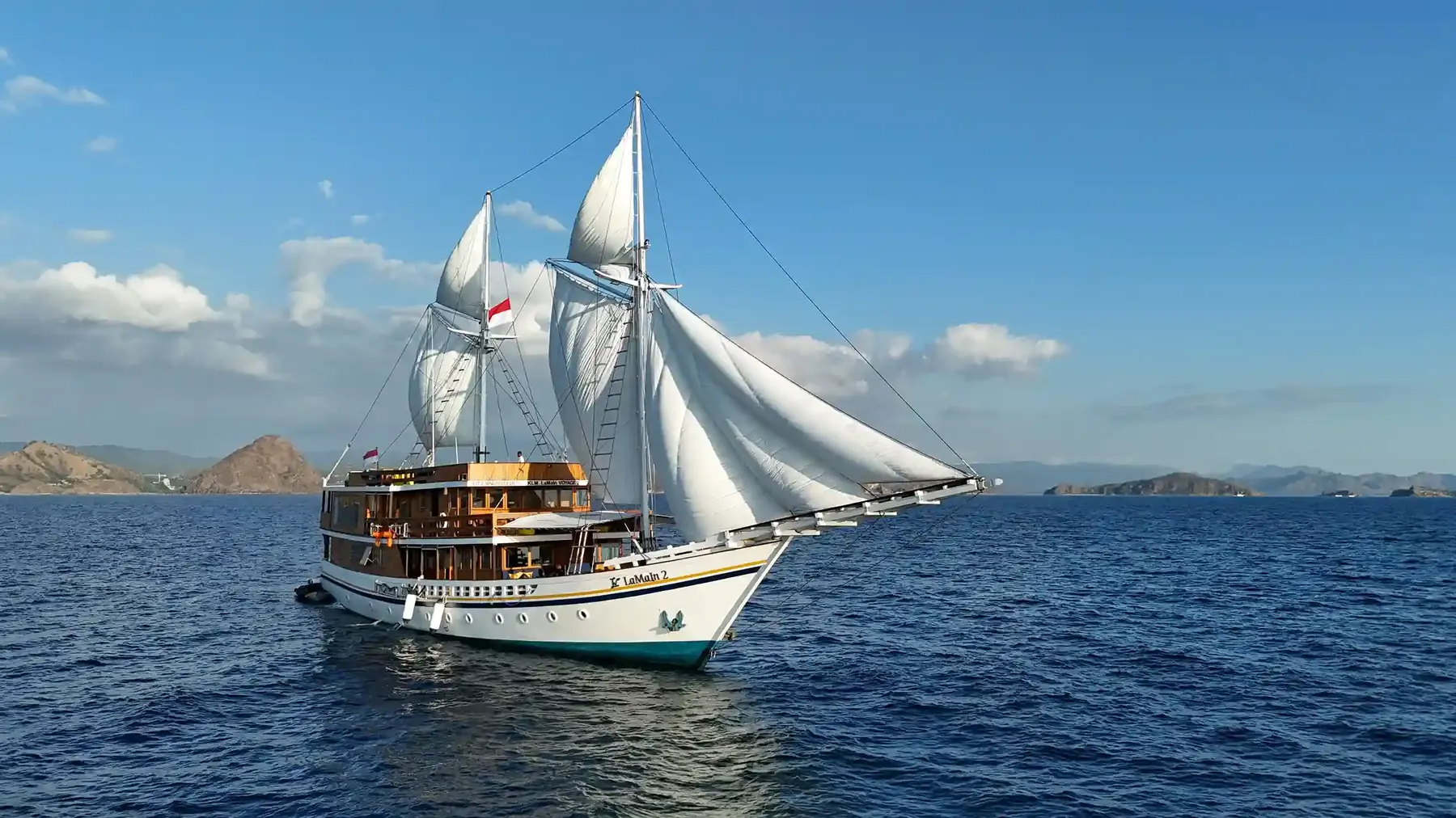 Wooden phinisi under full white sail on open blue water