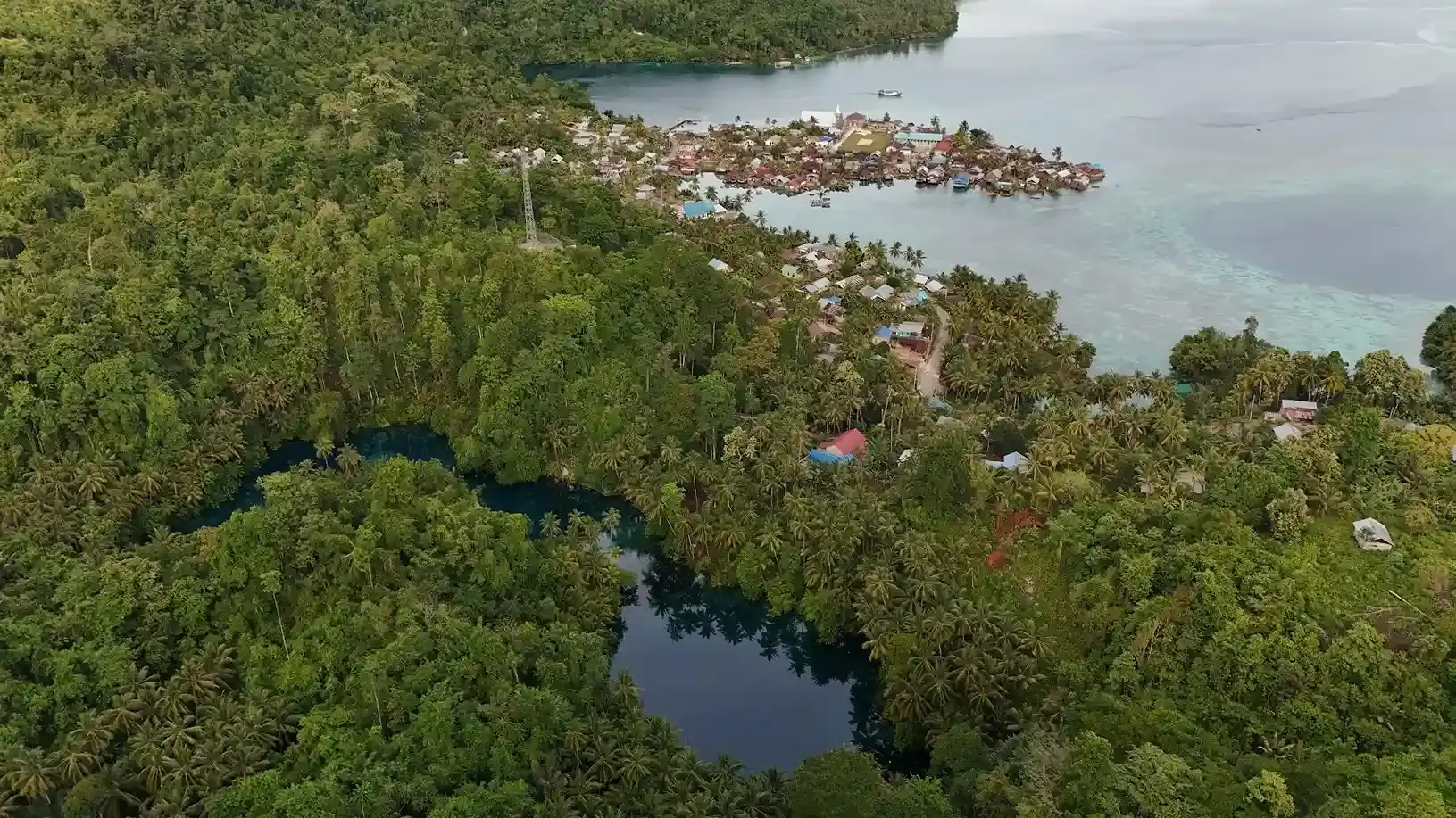 Aerial view of a coastal village on the water beside a jungle sinkhole lake